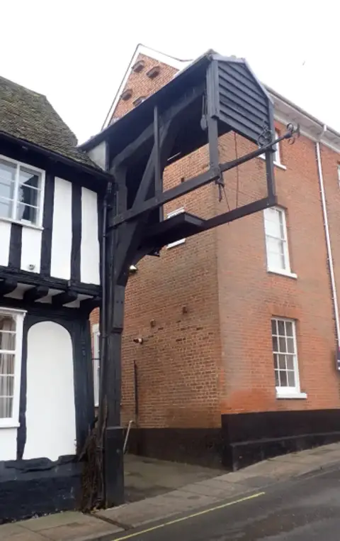Black timber weighing beam and its housing projecting from a brick wall above the street