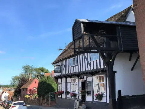 White timber-framed inn in sunshine with a black weighing beam projecting over the pavement
