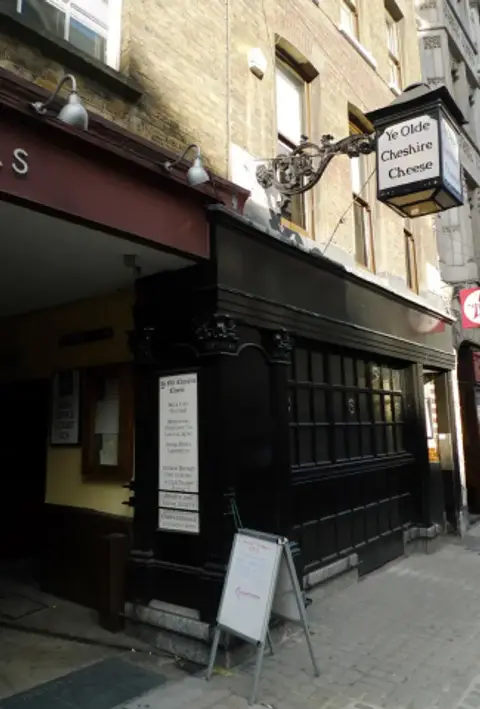 Black-painted pub frontage in a narrow court, with a white hanging lantern sign above
