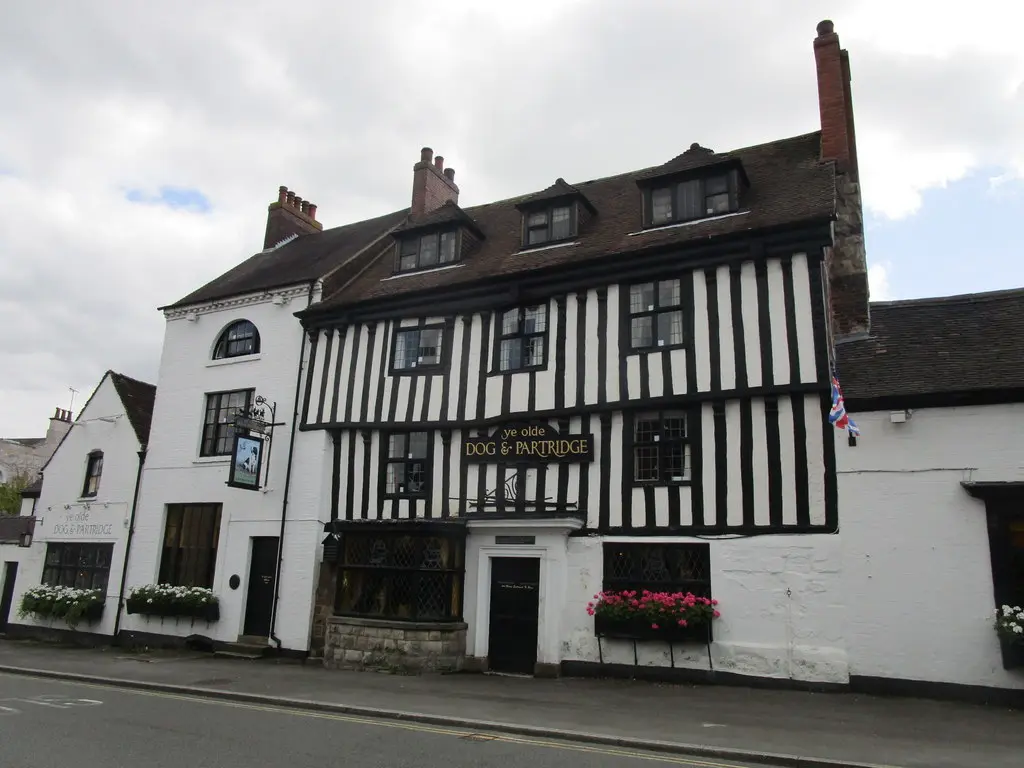 Timber-framed inn with window boxes of pink geraniums and a painted sign of a dog and partridge