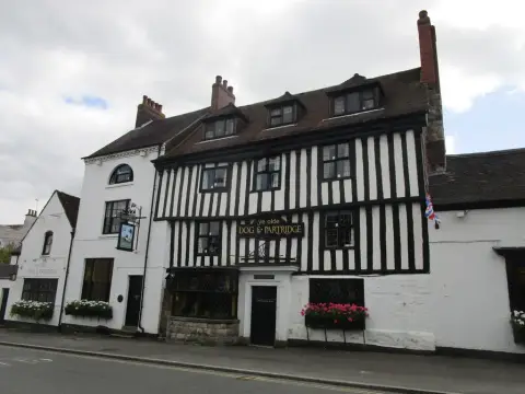 Timber-framed inn with window boxes of pink geraniums and a painted sign of a dog and partridge