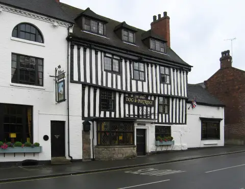 Tall close-studded timber-framed inn on a wet street, gold lettering across the frame