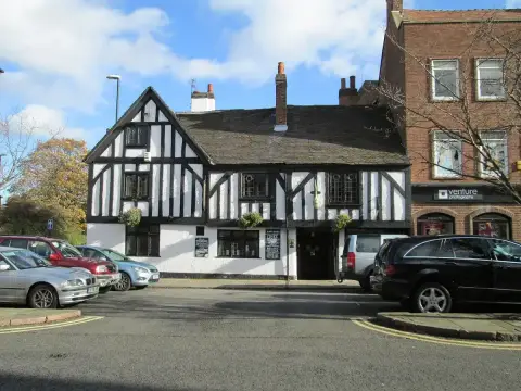 Timber-framed pub with a jettied upper floor and leaded windows, cars parked in front