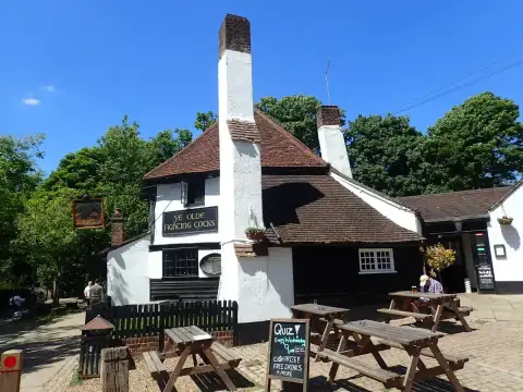 Low white-walled pub with a steep tiled roof, tall chimneys and picnic benches on the gravel outside