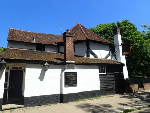 Side elevation of a white and black timbered pub with overlapping tiled roofs and a hanging sign