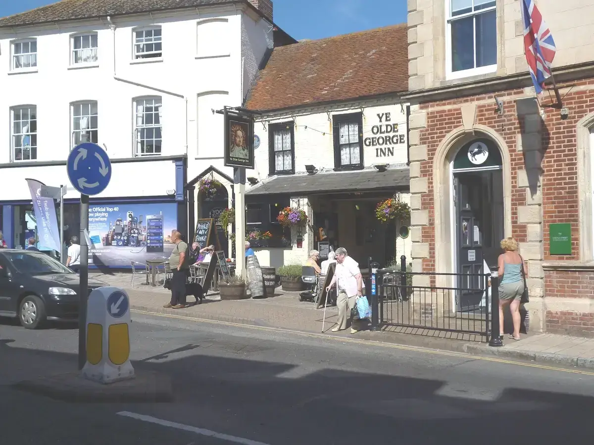White inn with a tiled roof and painted name lettering, set back behind a paved forecourt