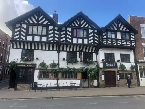 Timber-framed inn with three jettied gables in bright sun, metal tables on the pavement
