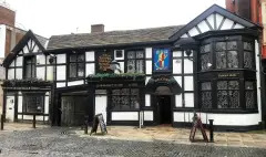 Black-and-white timbered pub with bay windows, a painted sign of a man with a scythe and dates
