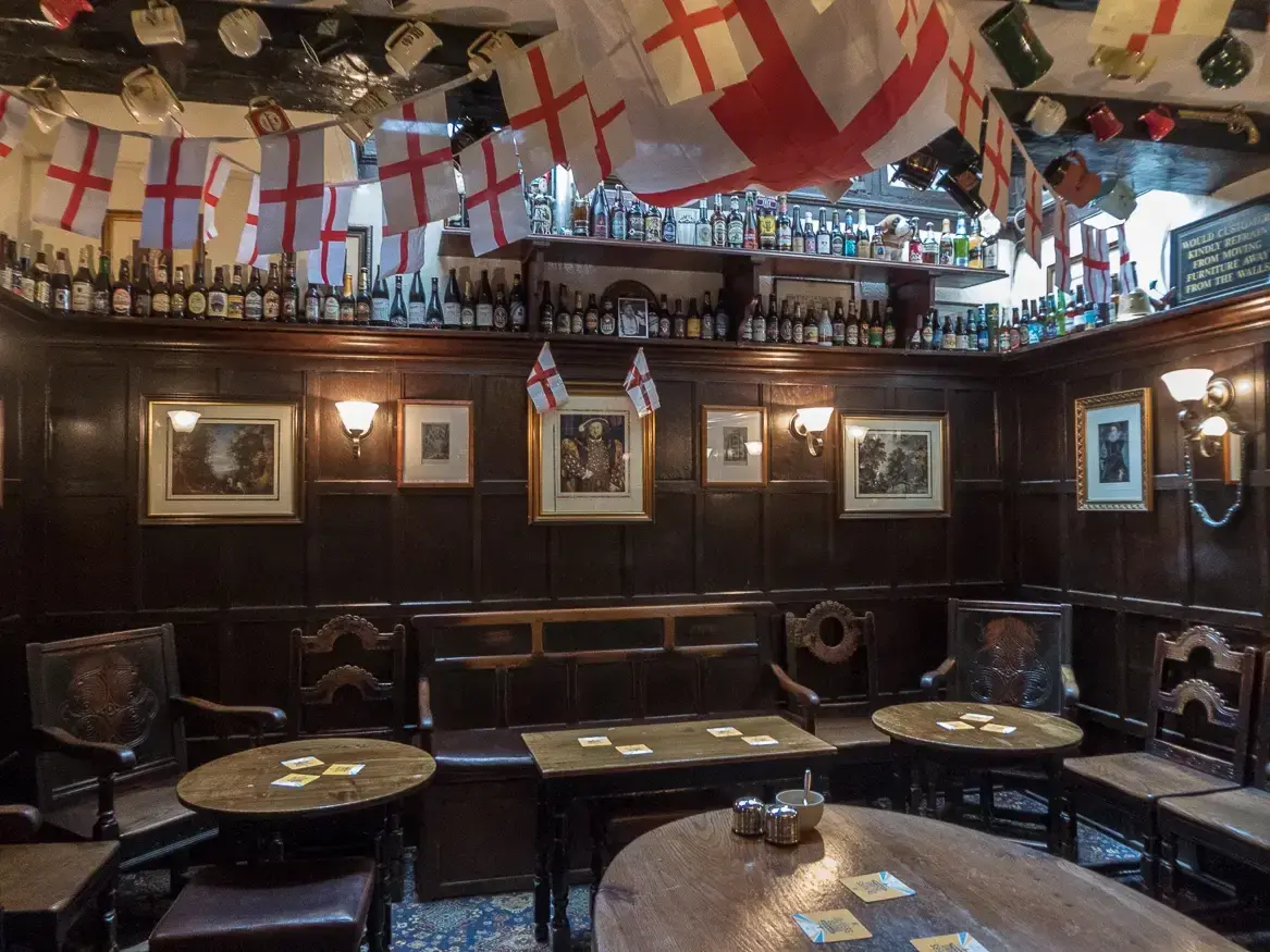Small oak-panelled room with settles and round tables, bottles and tankards along the picture rail