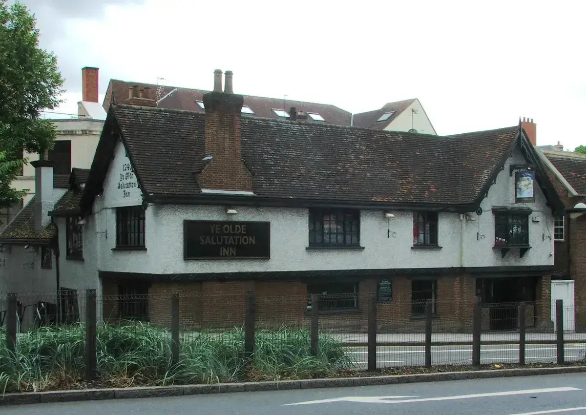 Long white rendered inn with a sagging tiled roof and painted name board, above a brick base