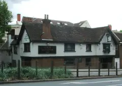 Long white rendered inn with a sagging tiled roof and painted name board, above a brick base
