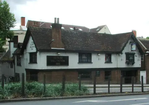 Long white rendered inn with a sagging tiled roof and painted name board, above a brick base
