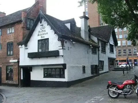 White gabled corner inn lettered 1240, with leaded windows and a tiled roof, on a cobbled street