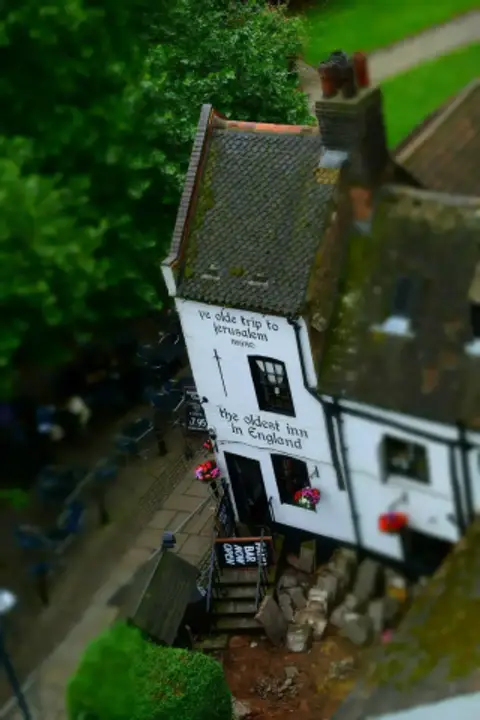 Whitewashed gable lettered with the inn's name and 1189, seen from above with tables in the yard