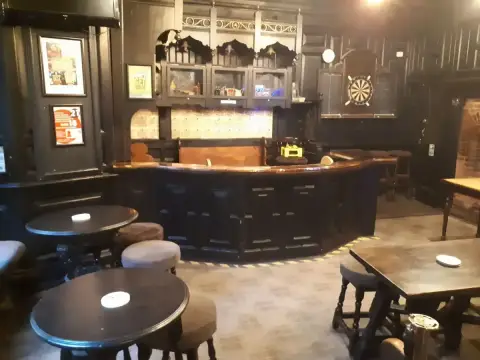 Dark panelled bar room with a curved copper-topped counter, low stools and a dartboard