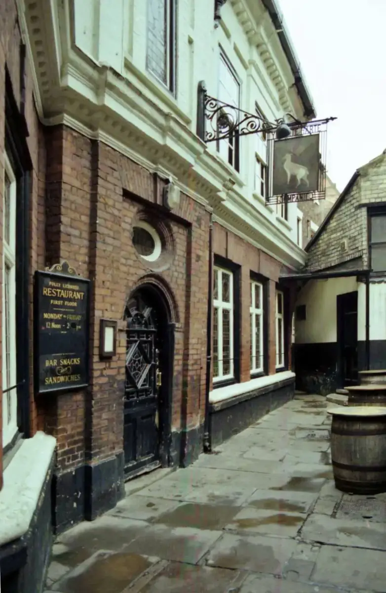The brick front of Ye Olde White Harte down its alley in 1982, arched door, hanging sign and a restaurant board