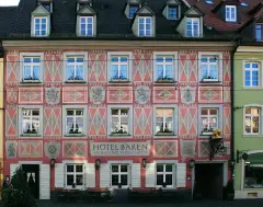 Pink and white painted front with coats of arms and dates, lettered Hotel Bären, tables set out below