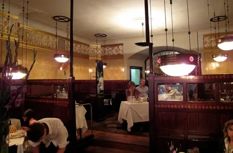 Panelled dining room with tiled walls, brass lamps and white-clothed tables in booths