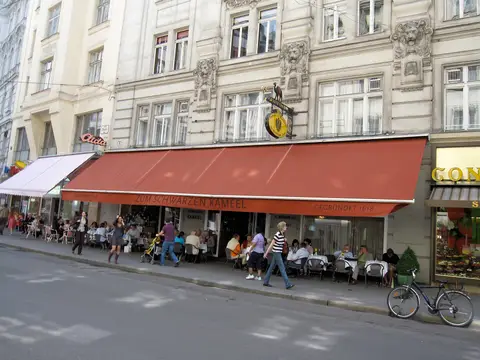 Red awning lettered Zum Schwarzen Kameel gegründet 1618 over pavement tables, camel sign above