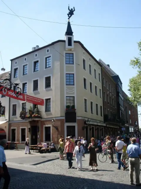 Rendered corner brewery house dated 1862 with a figure weather vane, benches on the square outside