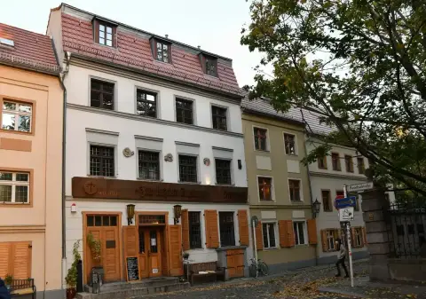 The same house in its street, a brown sign lettered seit 1621 and a bench beside the door